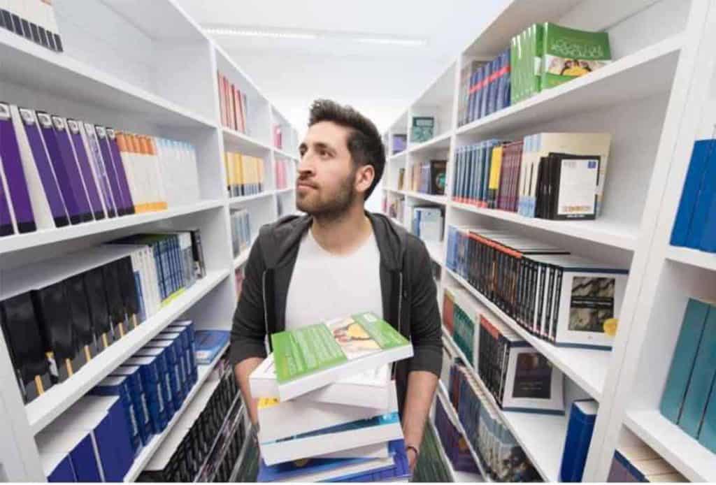 young male student carrying books in library to put them away