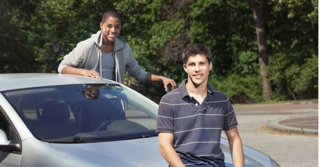 two diverse teenagers sitting on grey car