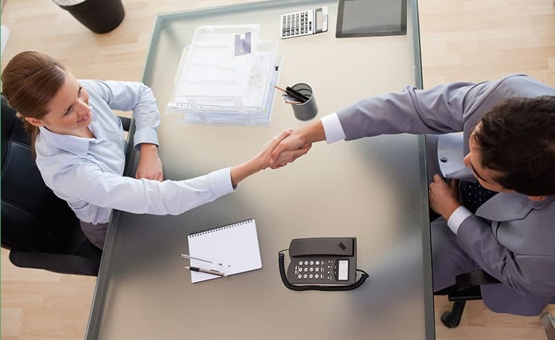 male and female dressed in business atire shaking hands over a desk in an office from an overhead view