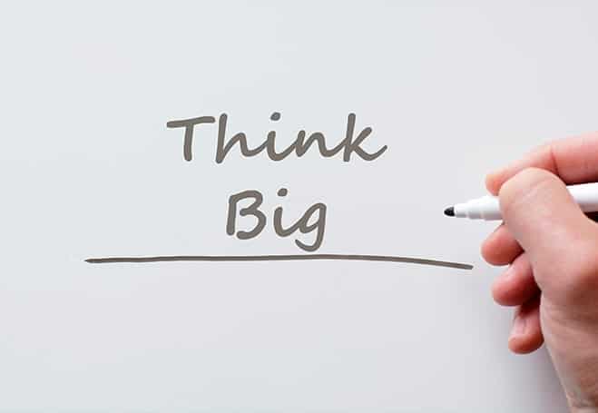 think big written in brown colour on white board with hand and felt pen in picture 