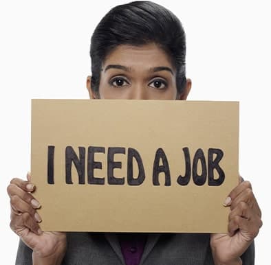 woman with dark hair holding a sign with black text on brown paper that says I need a job.