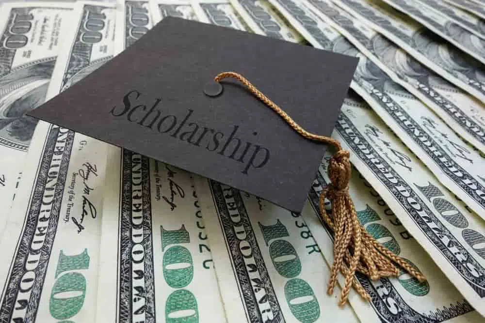 Home 15 black graduation cap with text scholarship on top of many 100 dollar bills