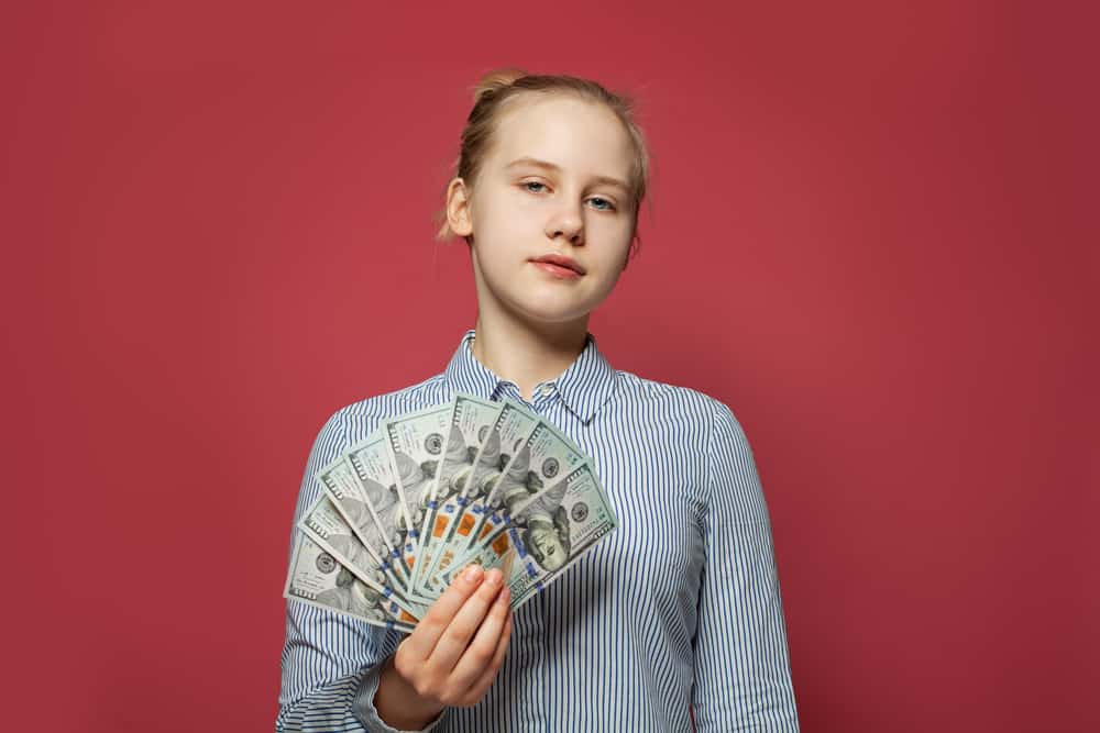 Teenage caucasion female holding a stack of money in her hand with red background