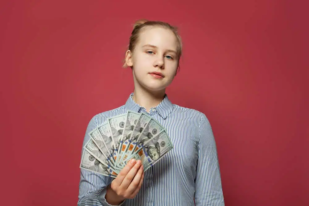 Home 7 Teenage caucasion female holding a stack of money in her hand with red background