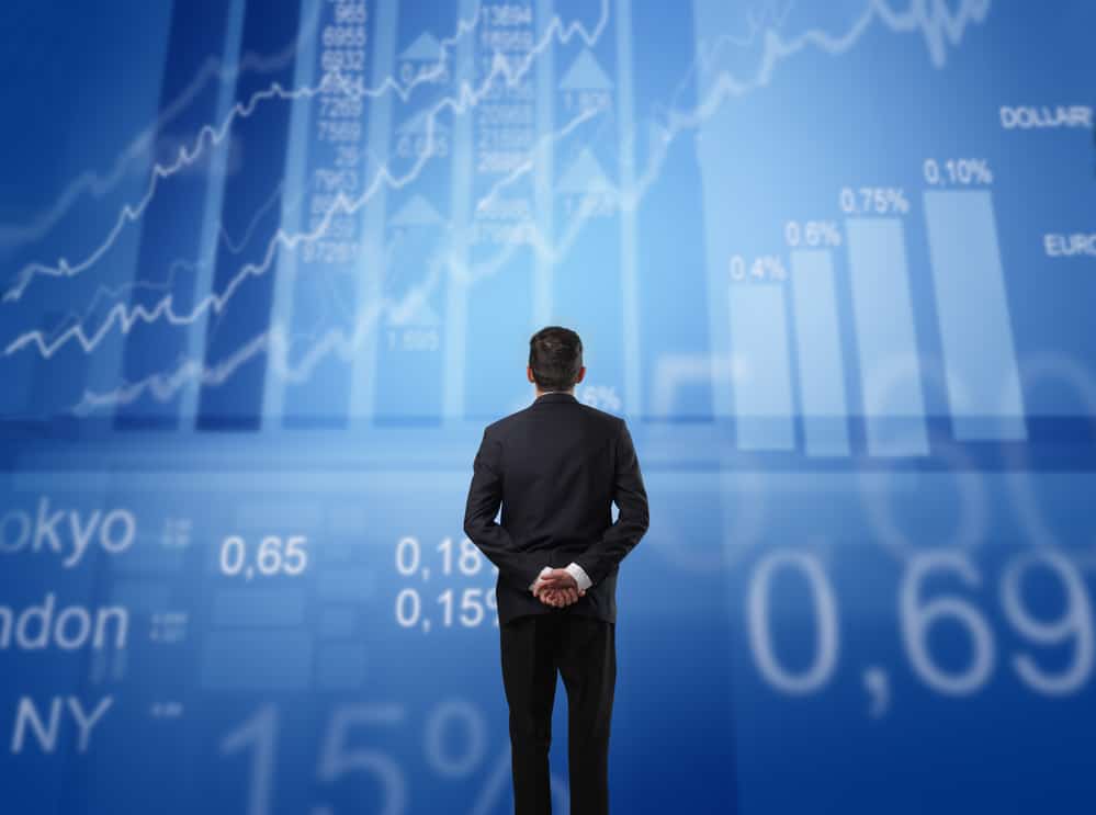 man in suit facing wall with stock market charts on blue background