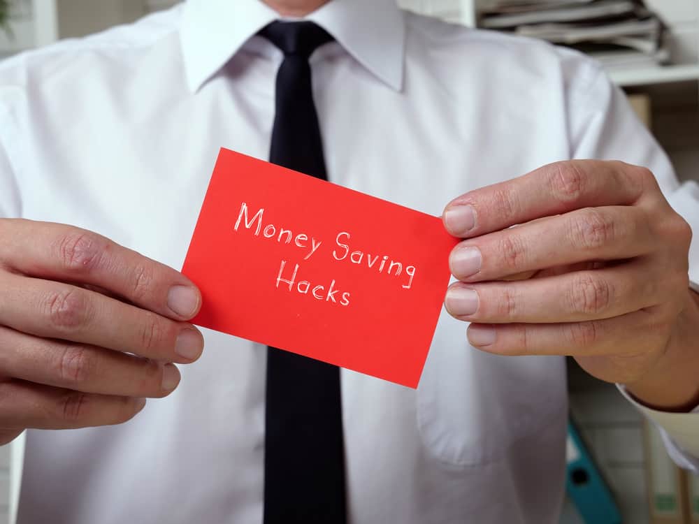 man in white shirt with black tie holding a red card that says money saving hacks