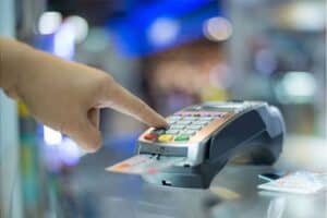 Credit card tips for students. A credit card in a machine for paying at checkout with finger punching in password.