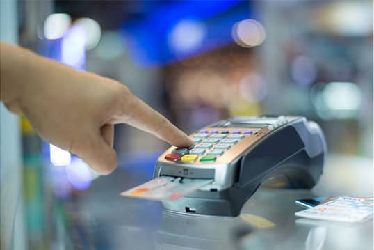 Credit card tips for students. A credit card in a machine for paying at checkout with finger punching in password.