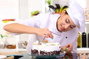 Young girl decorating a cake in a professional kitchen setting.