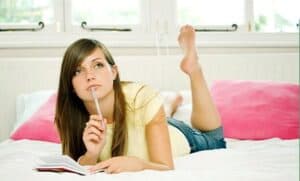 caucasian girl lying on bed with diary and pen wearing jeans thinking how much money should a teenager save