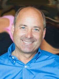 Smiling man in a blue shirt with a blurred background.