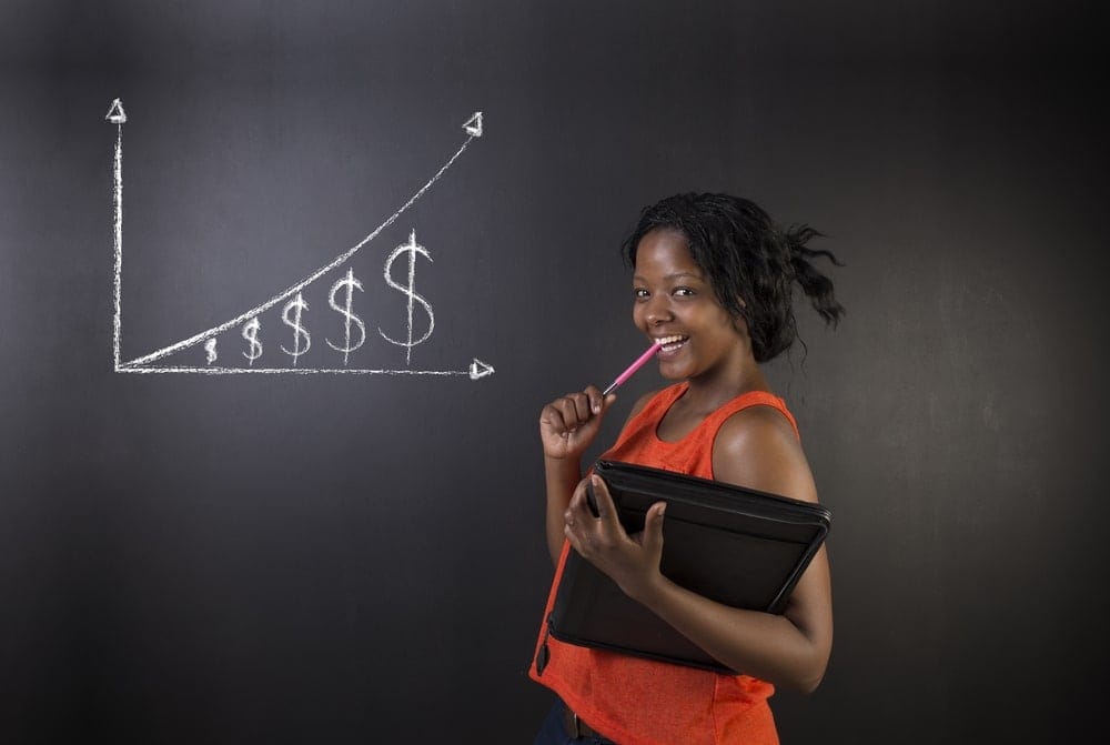 Teen girl smiling with a notebook and pencil, next to a rising financial graph on blackboard.