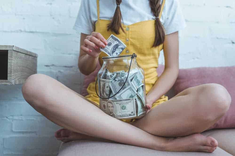 Young women wearing yellow and sitting on a chair with a jar of money bills
