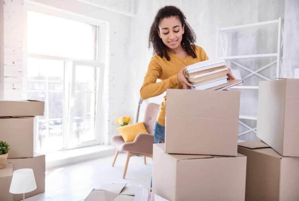 How much you should save before moving out, girl packing boxes of books