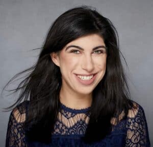 Smiling woman with dark hair wearing a navy lace top against gray background.