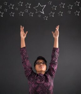 Young dark skinned woman reaching high for stars as in star goals