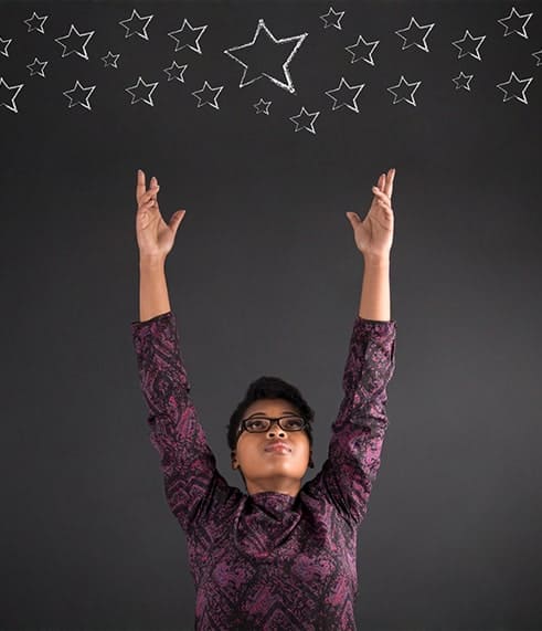 Young dark skinned woman reaching high for stars as in star goals