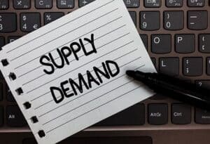 Supply demand written on lined notebook laying on a black keyboard for article what are supply and demand