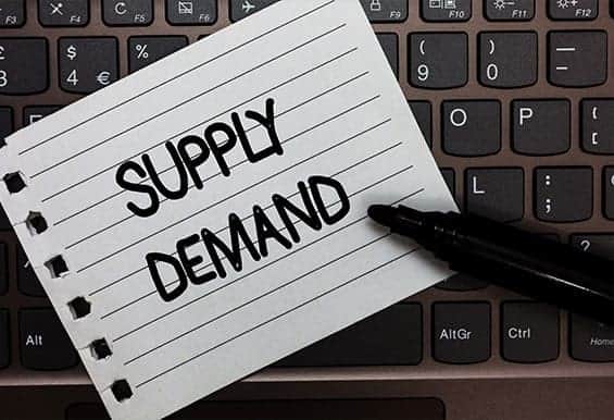 Supply demand written on lined notebook laying on a black keyboard for article what are supply and demand