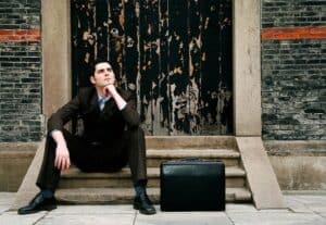 business man wearing suit sitting on stairs looking at sky thinking with a blag bag on the ground