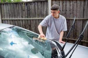 Teenage boy washing a car as part of a car detailing business