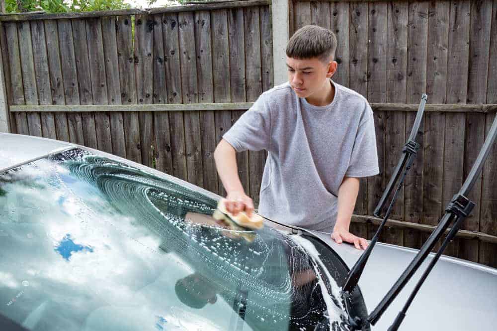 Teenage boy washing a car as part of a car detailing business
