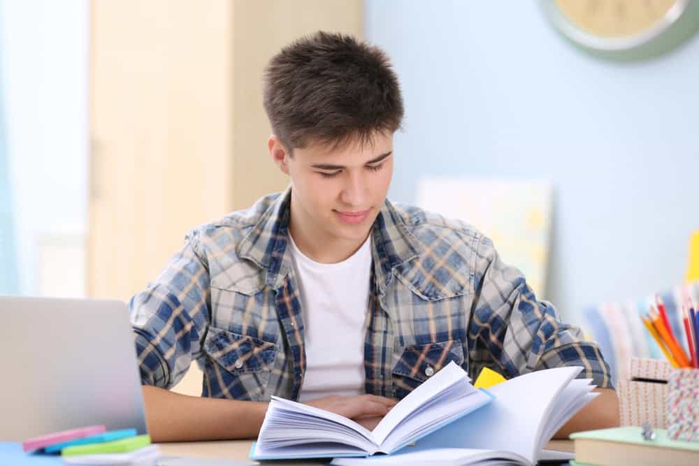 Teenager studying at home with an open book, representing the AI prompts for school guide