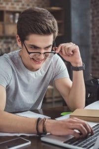 Smiling teenage boy in eyeglasses using a laptop, representing the Copilot guide for teens