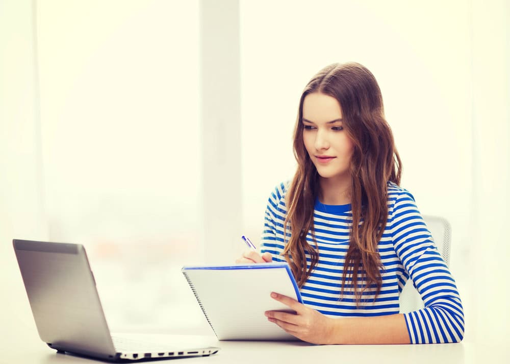 Teenage girl reviewing her college application notes with a laptop, representing the AI prompts for college applications guide