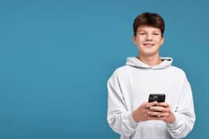 Smiling teenage boy holding a smartphone, representing the Gemini guide for teens