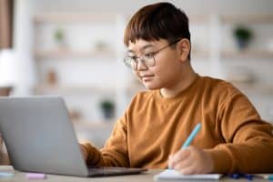Teenage boy at a laptop writing notes, representing the AI prompts for teens guide
